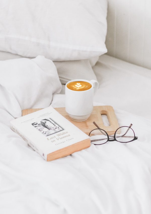 a book, a cup of coffee and some glasses on a bed
